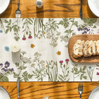 Table setting with floral placemat, bread, and candles on a wooden table.