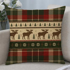 A square throw pillow with a festive Christmas pattern featuring moose silhouettes, pine trees, snowflakes, and plaid borders in red, green, beige, and brown, resting on a light gray sofa.