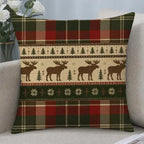 A square throw pillow with a festive Christmas pattern featuring moose silhouettes, pine trees, snowflakes, and plaid borders in red, green, beige, and brown, resting on a light gray sofa.