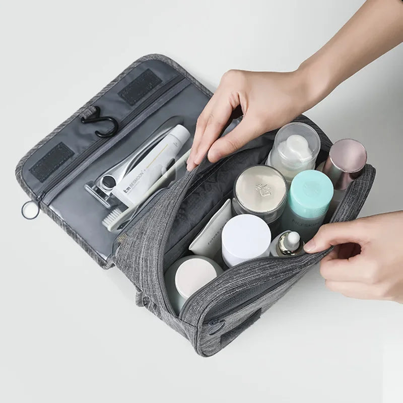 Gray travel toiletry bag with various items being organized by hands on a light gray background