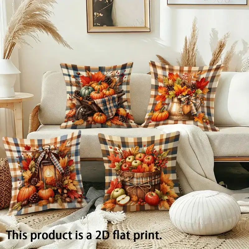 Four autumn-themed throw pillow covers displayed on a beige sofa in a styled living room. The pillows feature fall harvest prints with pumpkins, apples, pinecones, and plaid borders.