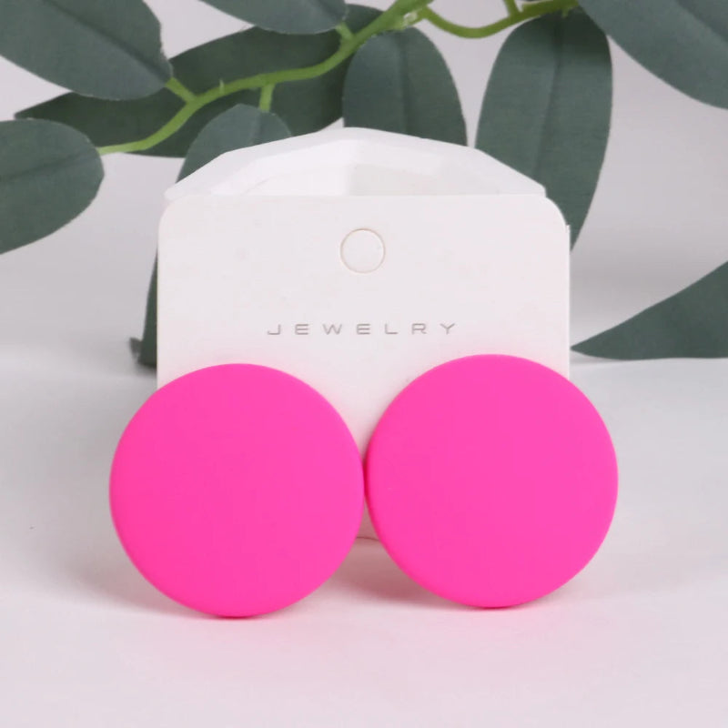Pink earrings on a white jewelry box with green leaves in the background