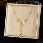 Gold necklace with a bow pendant on a beige display box.