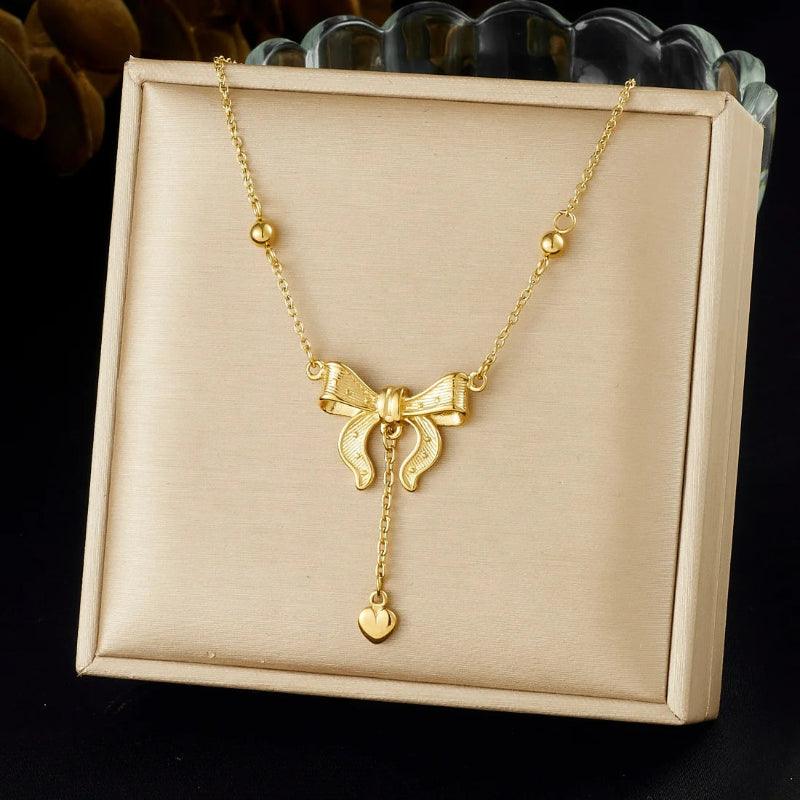 Gold necklace with a bow pendant on a beige display box.