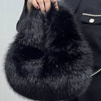 Black fur clutch held by a person wearing a dark coat with a light gray background