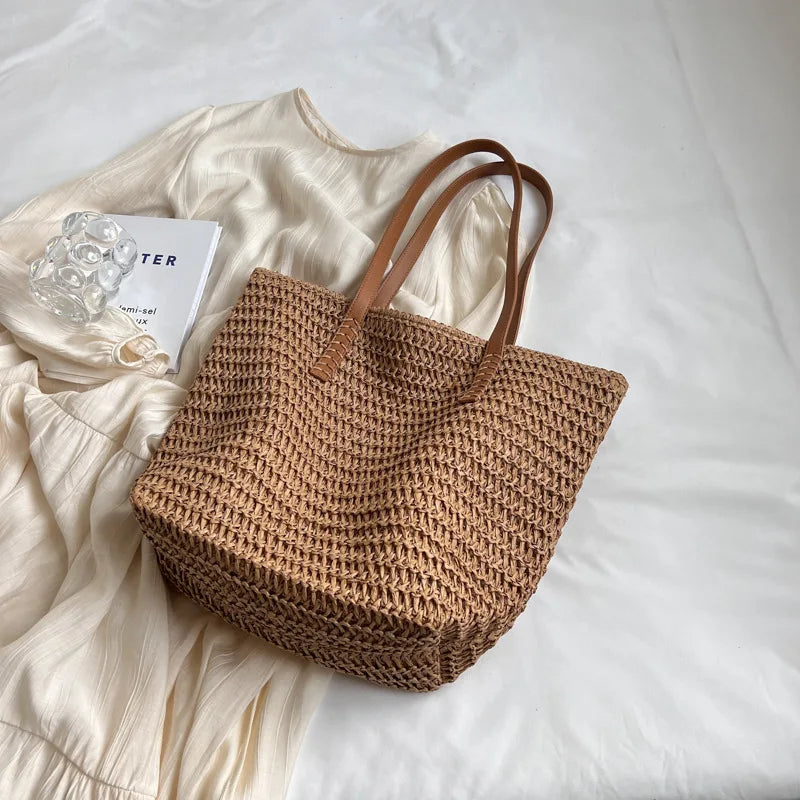 Brown woven tote bag on a white surface with a beige shirt and a book.