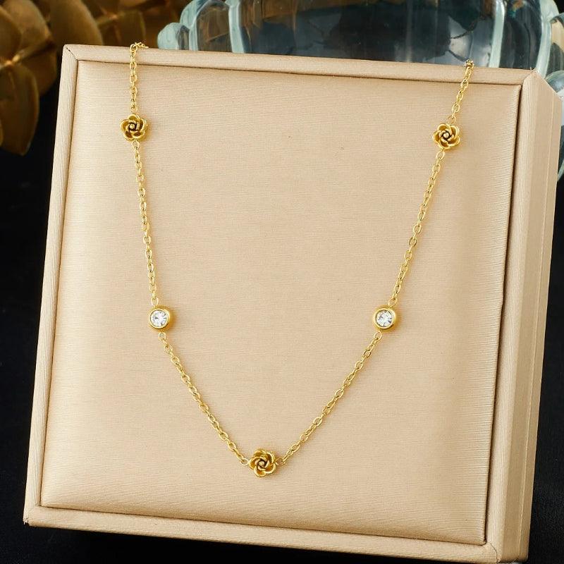Gold necklace with floral and round pendants on a beige display box.