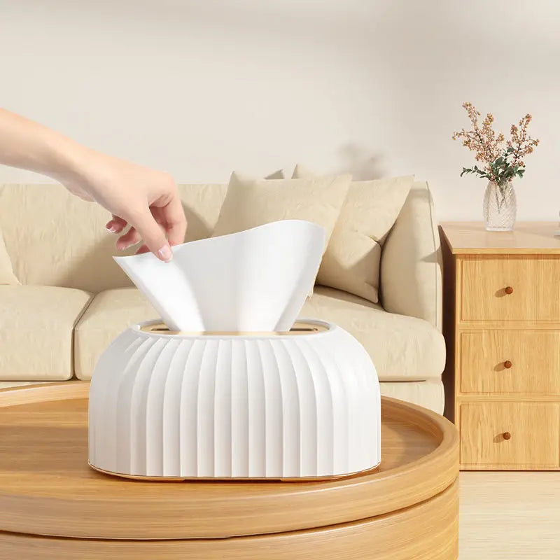 White tissue box on a wooden table with a hand reaching for tissues, in a living room setting.