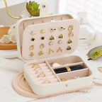 Beige jewelry organizer with earrings, rings, and a lip gloss on a light surface.