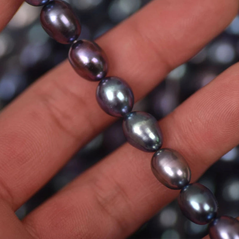 A close-up of a hand holding a strand of dark, iridescent baroque pearls. The pearls have a deep purple and blue-gray color with a glossy, metallic sheen.