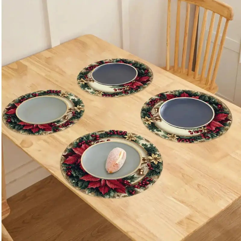 Four round holiday-themed placemats with a green wreath border and red berries, arranged on a light wood dining table with plates on top.
