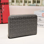 A dark gray zip-around wallet with an embossed monogram pattern, displayed on a white surface with a red box and books in the background.
