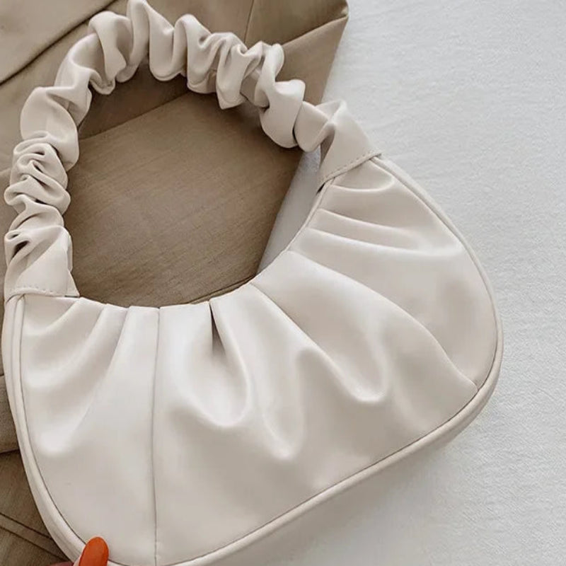 Beige pillow with ruffled edges held by a hand on a light surface.
