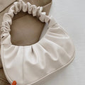 Beige pillow with ruffled edges held by a hand on a light surface.