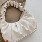 Beige pillow with ruffled edges held by a hand on a light surface.