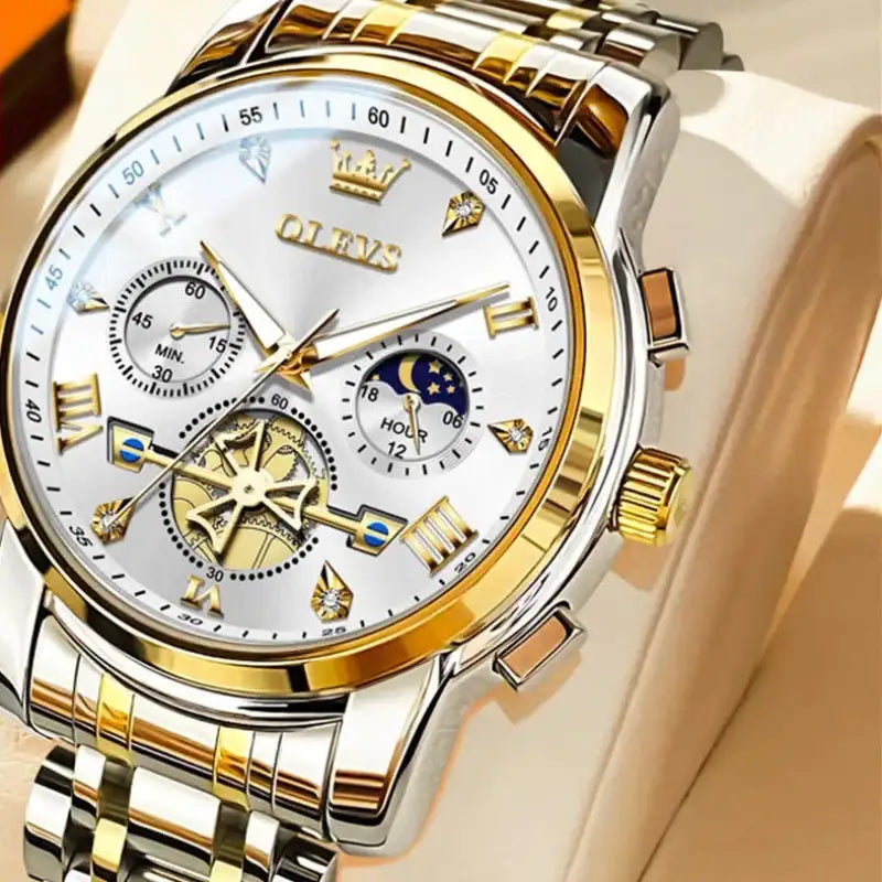 Gold and silver watch with detailed face on a beige background, featuring OLEVS branding.