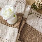 Close-up of a textured fabric with a white rose and dried flowers on a wooden surface.