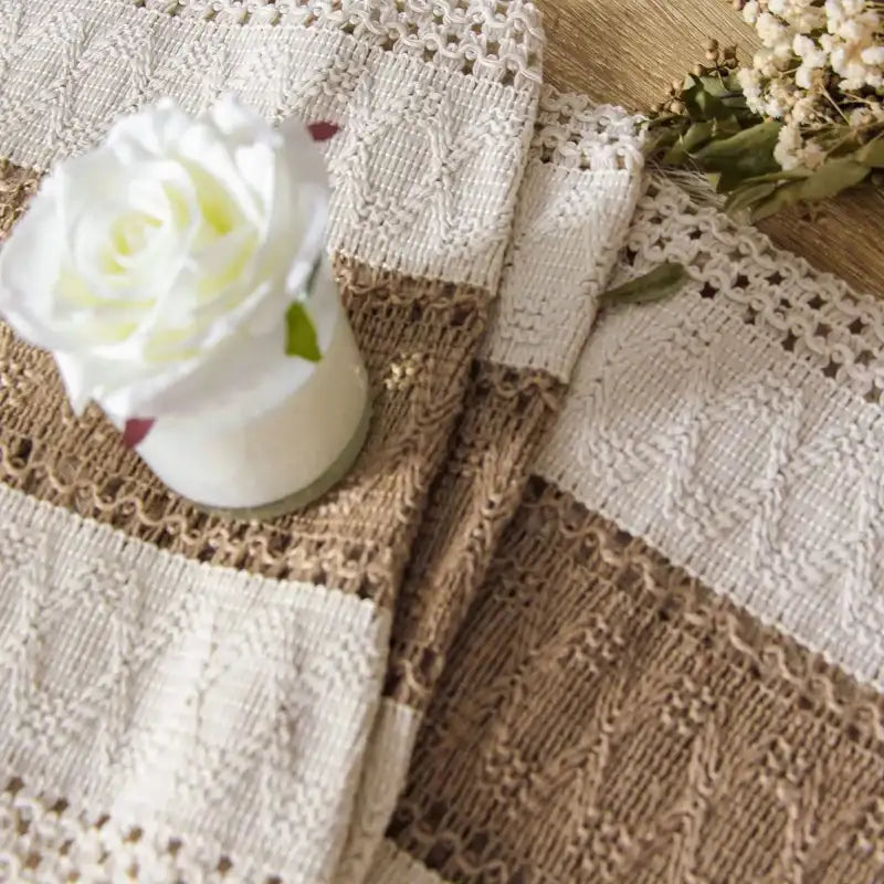 Close-up of a textured fabric with a white rose and dried flowers on a wooden surface.