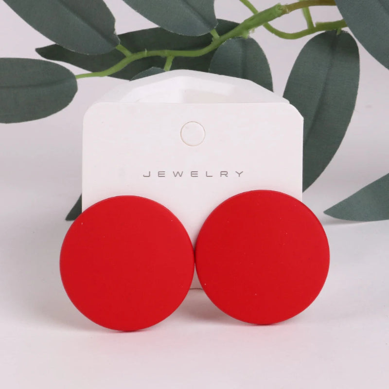 Red circular earrings on a jewelry card with green leaves in the background