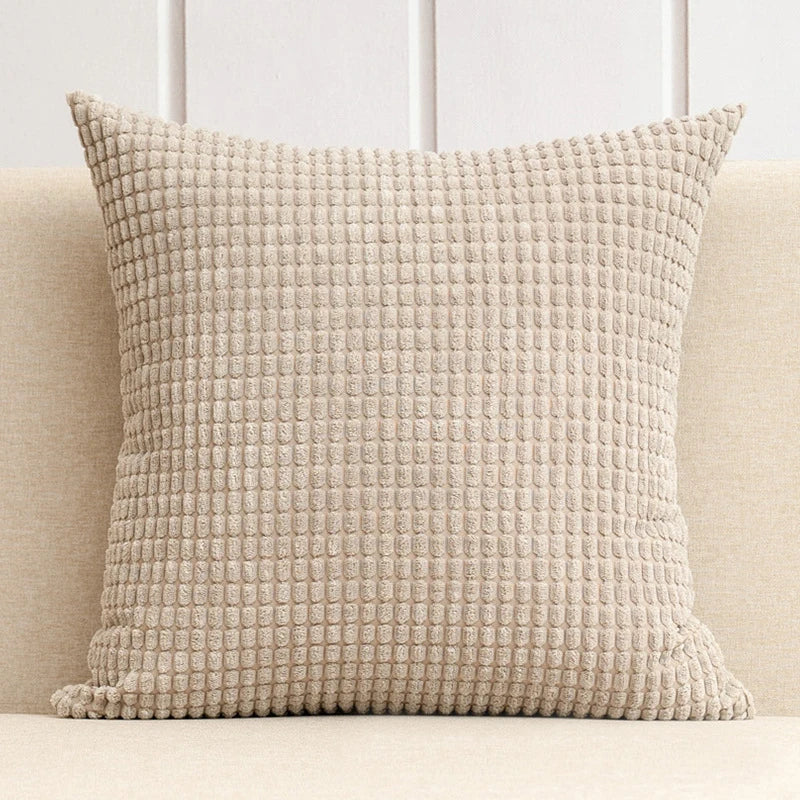 Textured beige pillow on a light-colored sofa with a neutral background