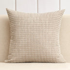 Textured beige pillow on a light-colored sofa with a neutral background