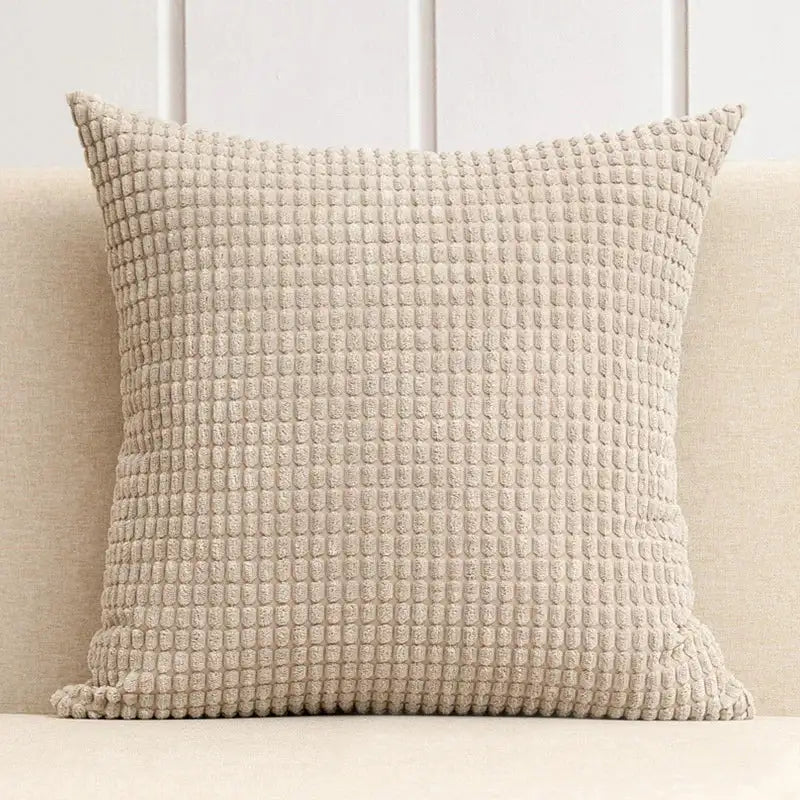 Textured beige pillow on a light-colored sofa with a neutral background