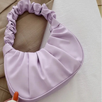 A light purple crescent-shaped shoulder bag with a gathered, ruched handle, styled on a beige blazer over a white fabric background.