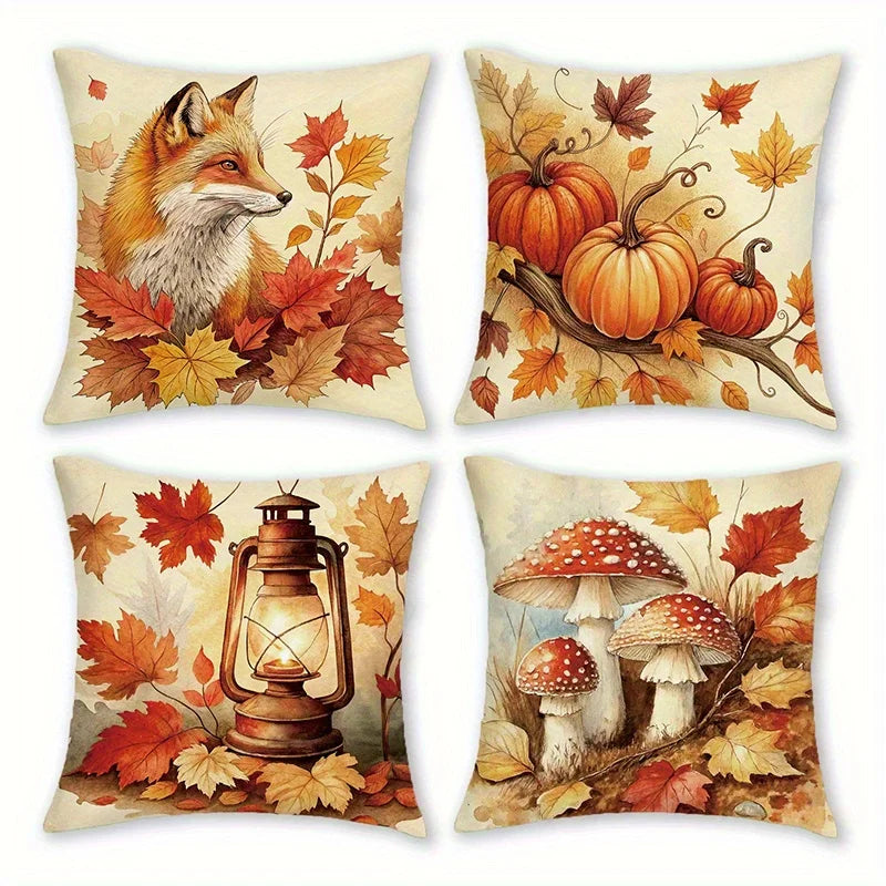 Four square decorative throw pillows arranged in a 2x2 grid, each printed with a different autumn-themed illustration: a fox among leaves, pumpkins on a branch, a lantern surrounded by leaves, and red-and-white mushrooms with leaves. The pillows have a warm cream background and are shown on a plain white background.