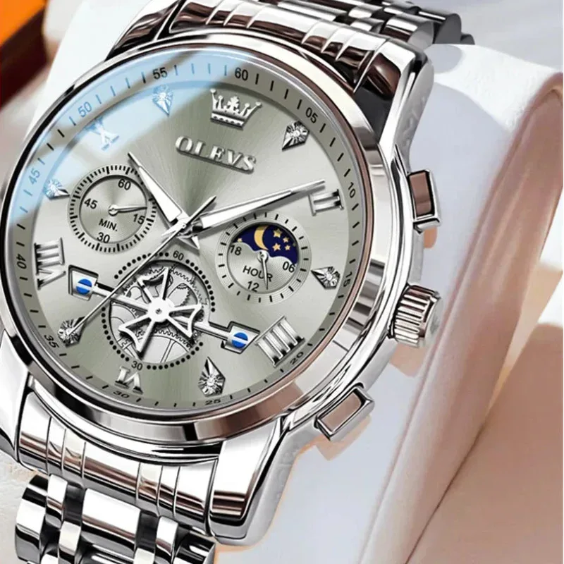 Silver wristwatch with detailed face on a white cushion, brand 'OLEVS' visible.