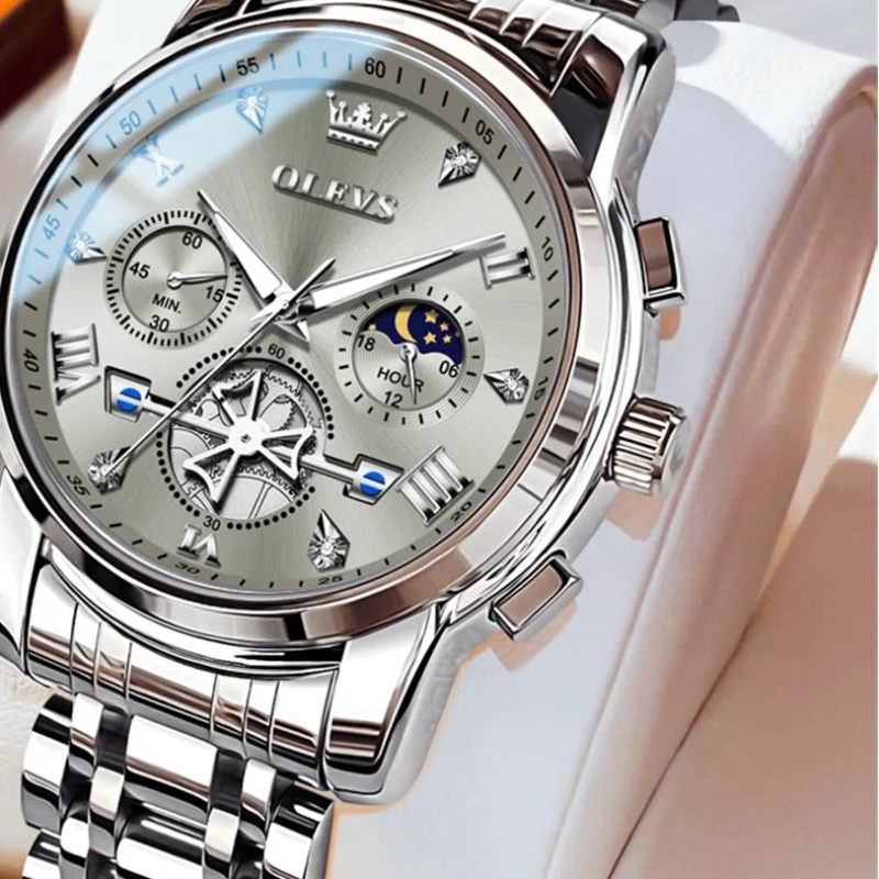 Silver wristwatch with detailed face on a white cushion, brand 'OLEVS' visible.