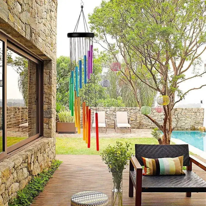 Colorful wind chime hanging outside a stone building with a garden and pool in the background.