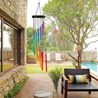 Colorful wind chime hanging outside a stone building with a garden and pool in the background.