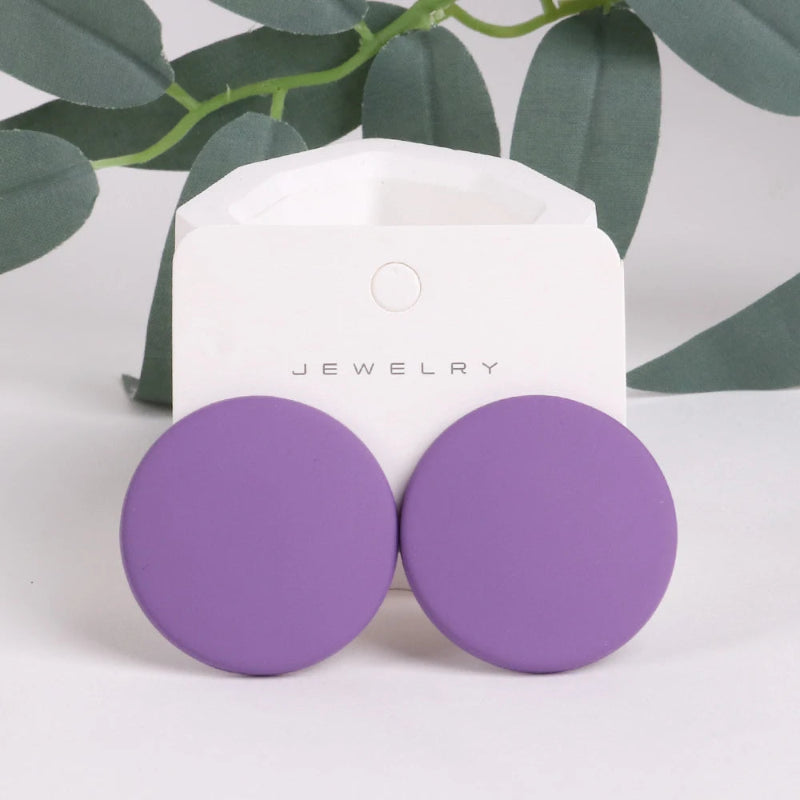 Purple round earrings on a jewelry card with green leaves in the background