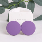 Purple round earrings on a jewelry card with green leaves in the background