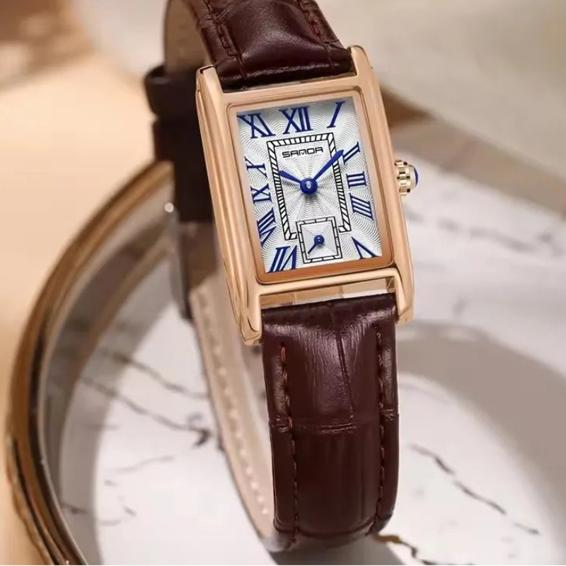 Watch with brown leather strap and gold case on a marble surface, brand 'SANDA' visible.