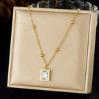 Gold necklace with a square pendant on a beige display box.