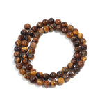 A coiled strand of polished tiger's eye beads in shades of brown, gold, and black, arranged in a circle on a white background.