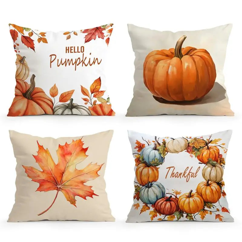 Four square decorative throw pillows arranged in a 2x2 grid on a white background. The designs feature autumn fall themes: one says 'Hello Pumpkin' with pumpkins and leaves, one shows a large orange pumpkin, one has a large orange maple leaf, and one says 'Thankful' with a wreath of pumpkins and gourds.