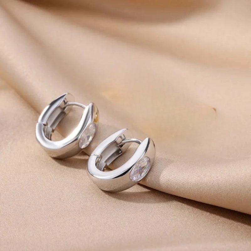 Pair of silver hoop earrings on a beige fabric background