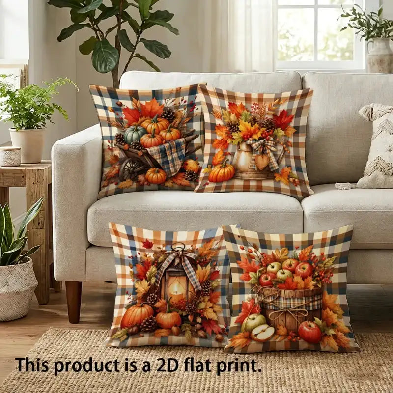 Four decorative throw pillows with a fall harvest and autumn plaid design are arranged on a beige sofa in a living room setting. The pillows feature colorful prints of pumpkins, gourds, apples, pinecones, and lanterns over a tan and brown buffalo plaid background.