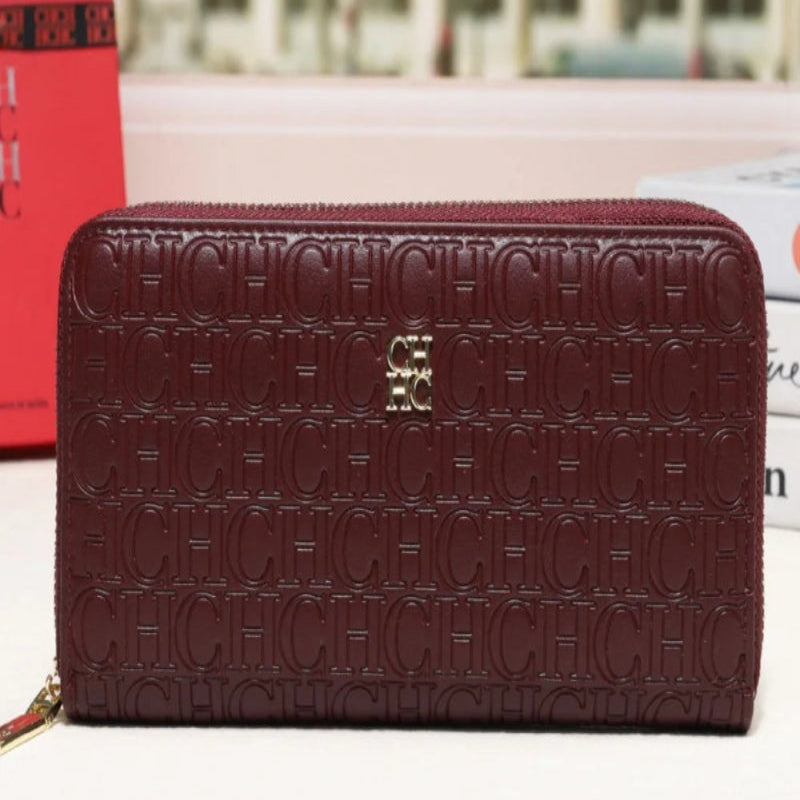 A burgundy monogram zip-around wallet with a gold-tone logo clasp, displayed on a white surface with a blurred city street background.