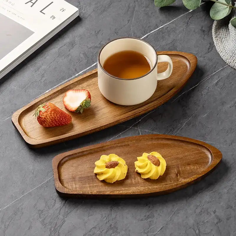 Wooden trays with a cup of tea, strawberries, and yellow pastries on a gray surface.
