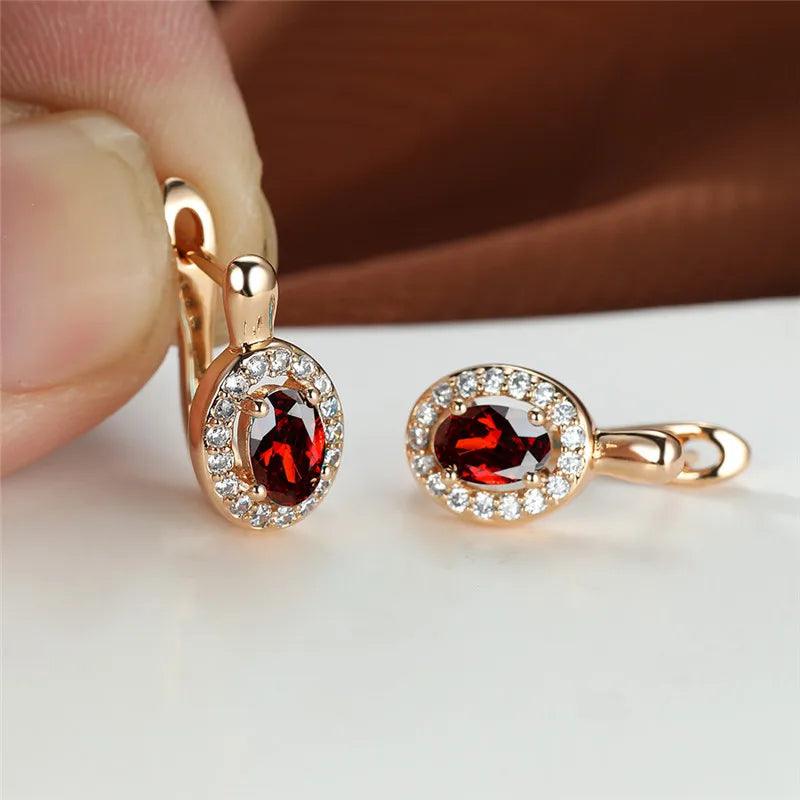 Rose gold earrings with red gemstones held by a hand on a white surface.