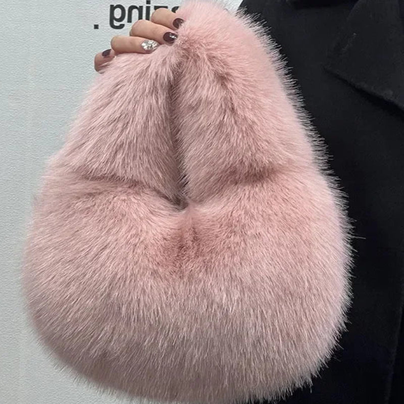 Pink fluffy handbag held by a person wearing a black coat against a light gray background.