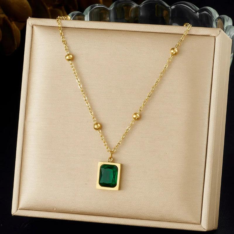 Gold necklace with a green gemstone pendant on a beige display box.