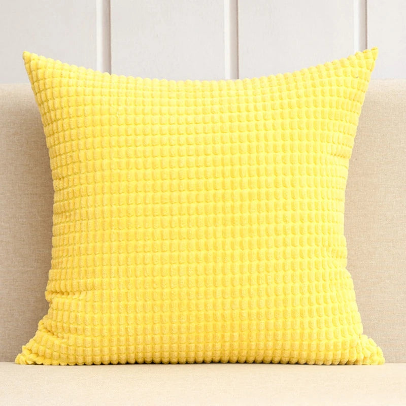 Yellow textured pillow on a beige couch against a white paneled wall.