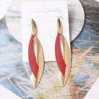 Gold and red earrings on a jewelry card with a natural background