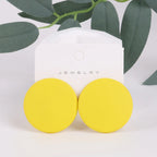 Yellow round earrings on a white jewelry card with green leaves in the background