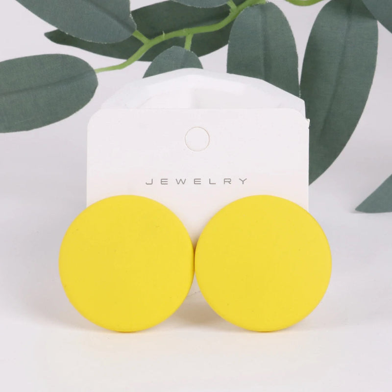 Yellow round earrings on a white jewelry card with green leaves in the background