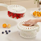 White kitchen strainer with tomatoes on a white surface, surrounded by fruits.